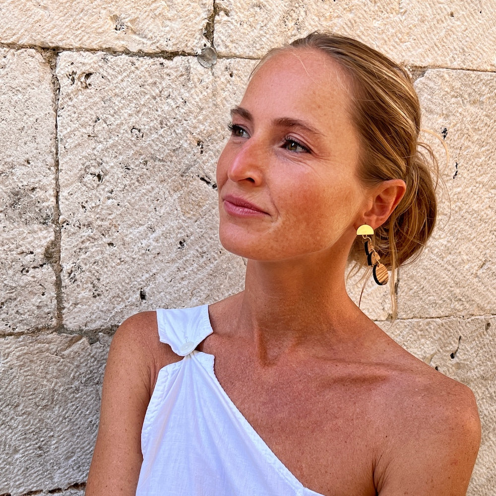 Olive Wood Moon Phase earrings on model in white shirt by stone wall