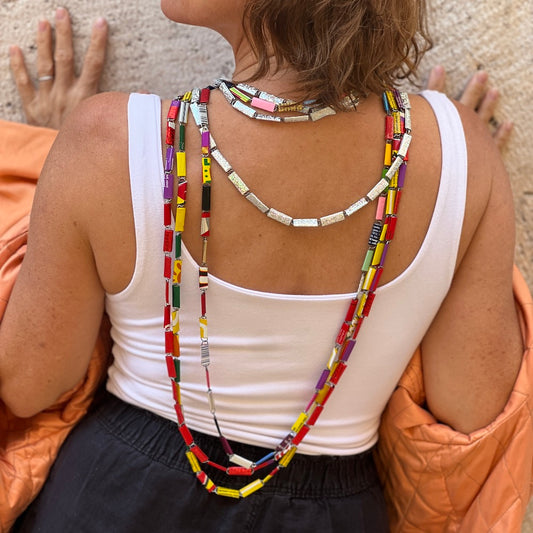 Colorful upcycled candy wrapper necklace on the back of a woman in white shirt and black pants 