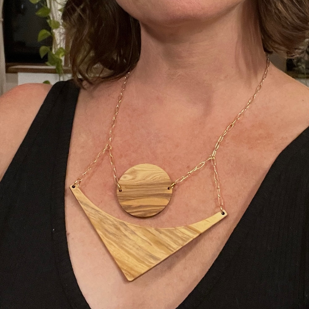 Olive wood circle and triangle pieces hang over each other on a gold chain, on designer Stacey Shevlin