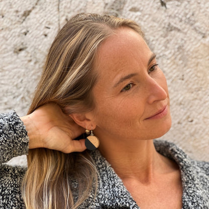 Model wearing cork earrings with black paint on them by stone wall