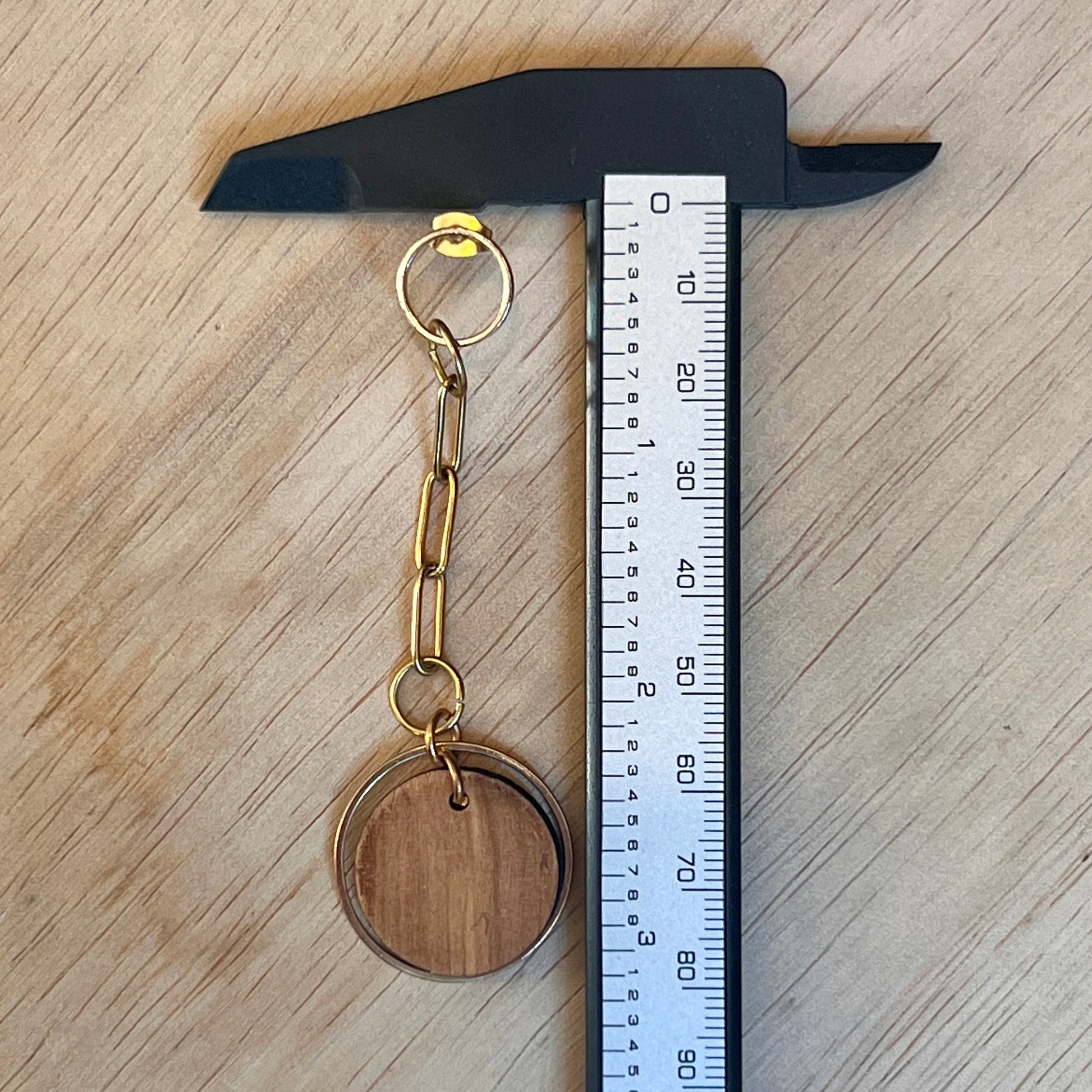 Chain link earring with olive wood circle on the end, on a surface next to a ruler showing 3 inches long