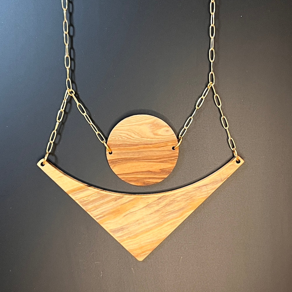 olive wood circle and arrow joined stacked by gold paperclip chain on black background by Madera Design Studio