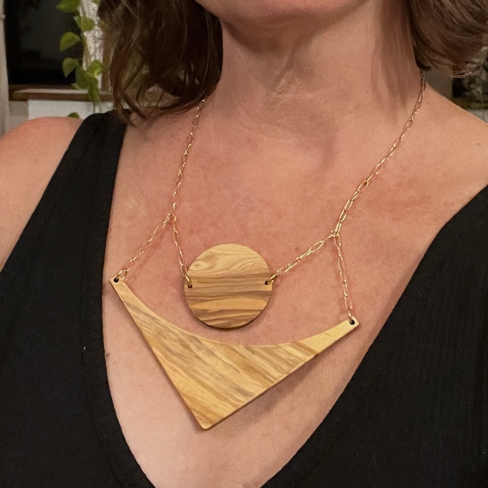 handcrafted olive wood necklace. A circle and arrow shape hang low on the chest on a gold plated chain. 