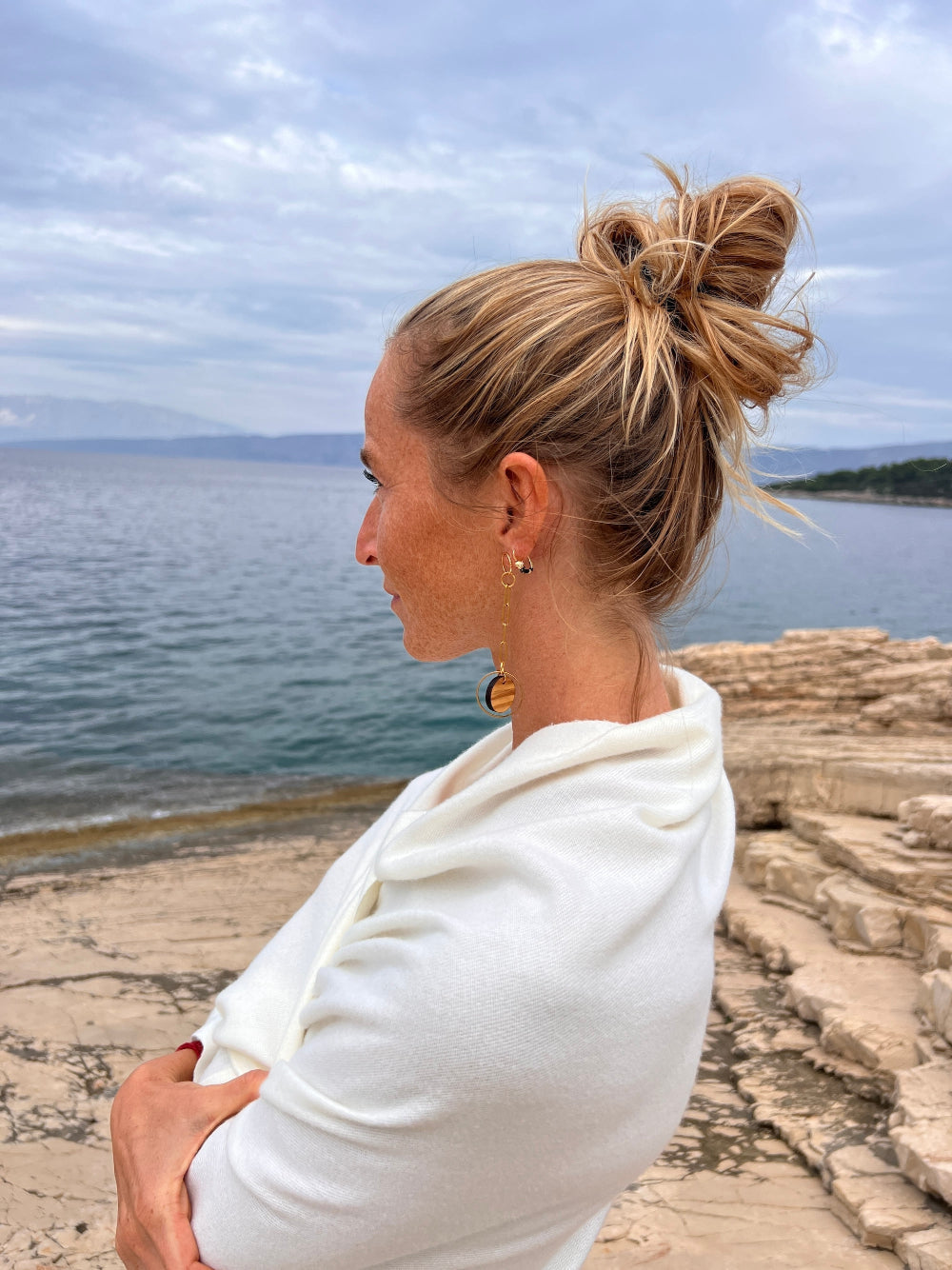 Woman staring at the sea in a white scarf, wearing olive wood and gold chain link earrings by Madera Design Studio